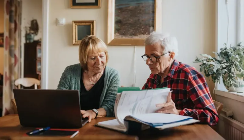 Une couple consulte des documents et s'aide d'un ordinateur portable.