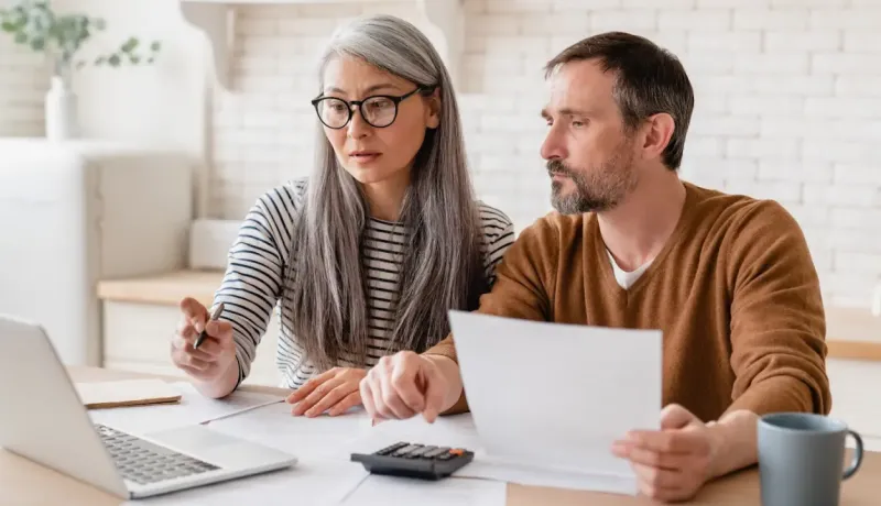 Un couple utilise un ordinateur portable et une calculatrice pour faire ses comptes à la maison.