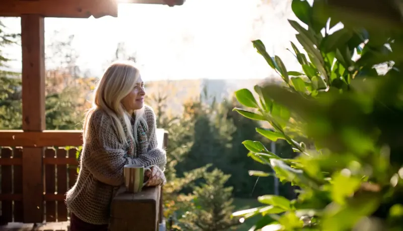 Une femme assise sur un porche, tenant une tasse de café, profitant d'un moment de détente en plein air.