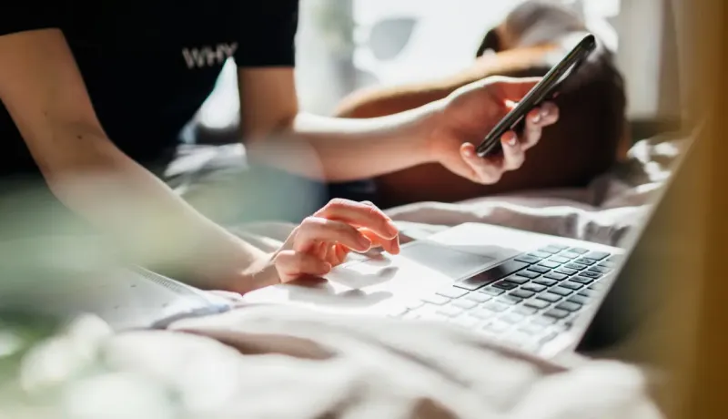 Gros plan montre main qui utilise téléphone et autre utilisant ordinateur.