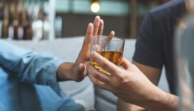 Une main repousse un verre d'alcool offert par une autre main.
