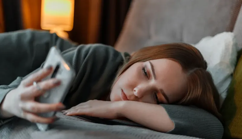 Une jeune femme est allongée, l'air pensif, regardant son téléphone portable.