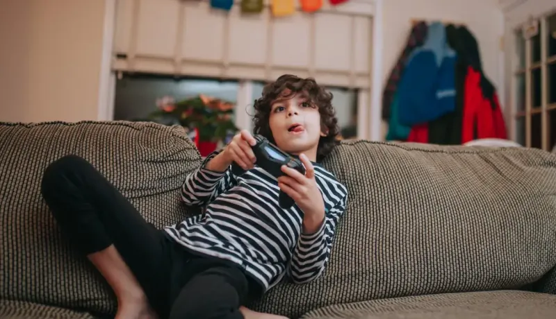 Un jeune garçon est assis sur un canapé, jouant à un jeu vidéo avec une manette.