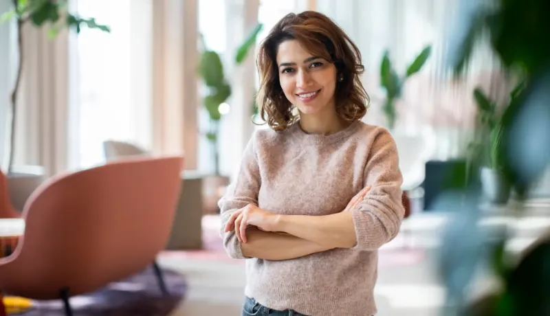 Une femme souriante aux bras croisés regarde la caméra.