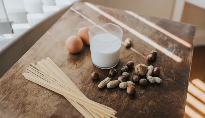 Des œufs, des pâtes, des noix et un verre de lait sont disposés sur une table en bois.