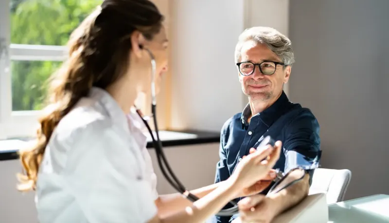 Une femme médecin prend la tension d'un homme d'âge mûr qui sourit.