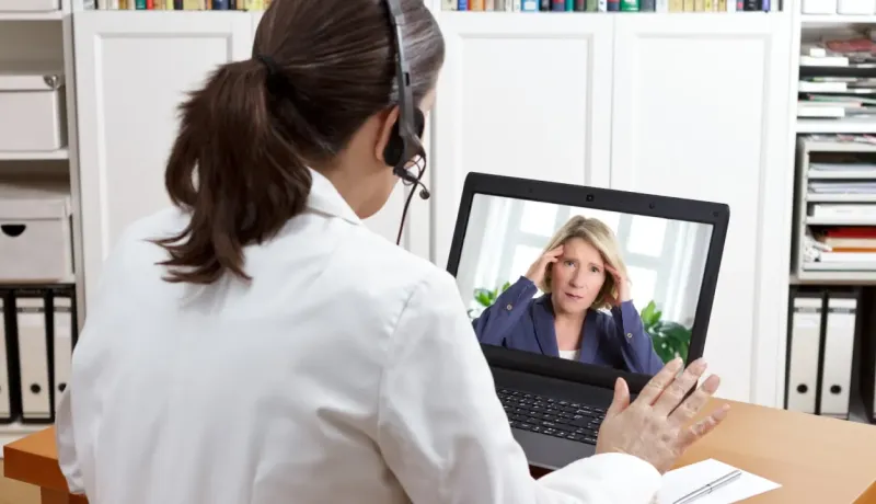 Une femme médecin en téléconsultation parle à une patiente visible sur l'écran de son ordinateur portable.