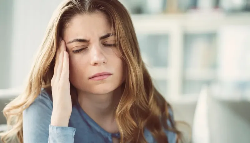 Gros plan d'une jeune femme les yeux fermés, les mains sur les tempes, souffrant de maux de tête.