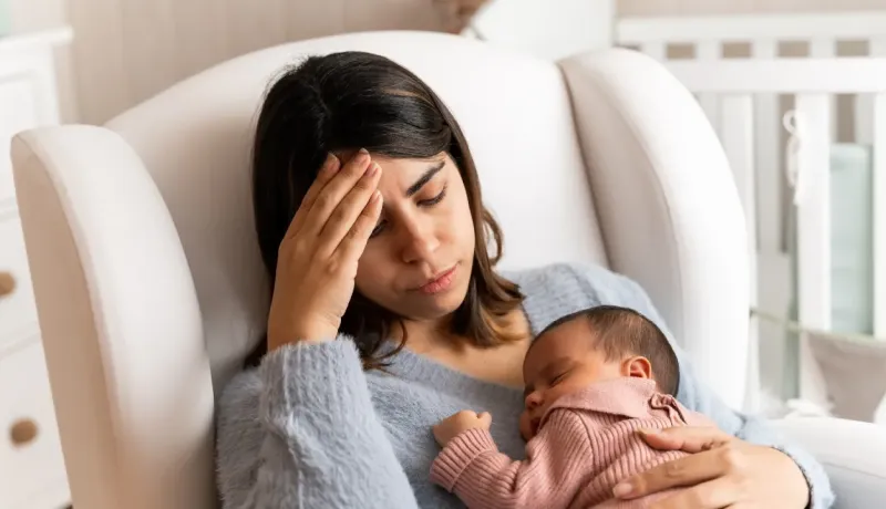 Une jeune mère l'air préoccupé tient son bébé endormi dans ses bras.