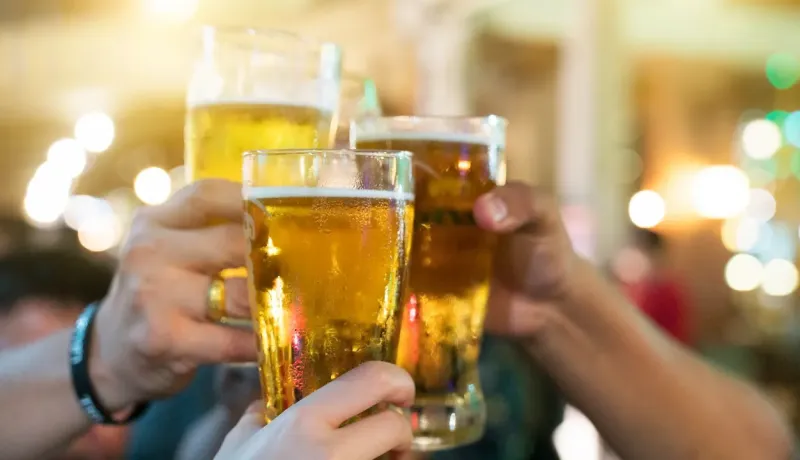 Des mains trinquent avec des verres remplis de bière blonde dans une ambiance festive et chaleureuse.