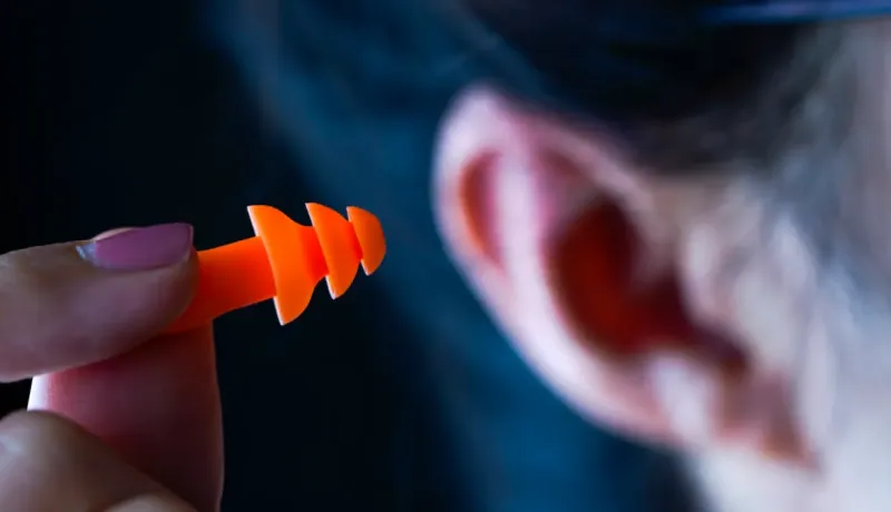 Gros plan d'une main insérant un bouchon d'oreille orange dans une oreille, pour la protection auditive.