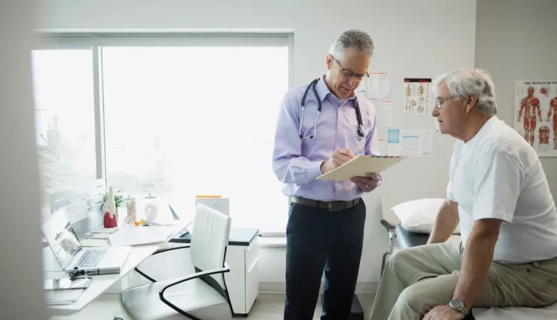 Un médecin en blouse consulte un patient âgé assis sur une table d'examen dans son cabinet.