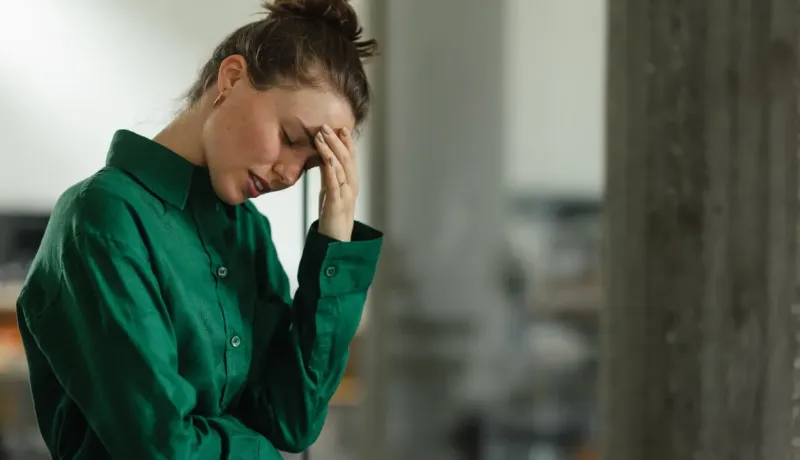 Une jeune femme aux cheveux attachés, vêtue d'une chemise verte, tient sa tête l'air affligé.
