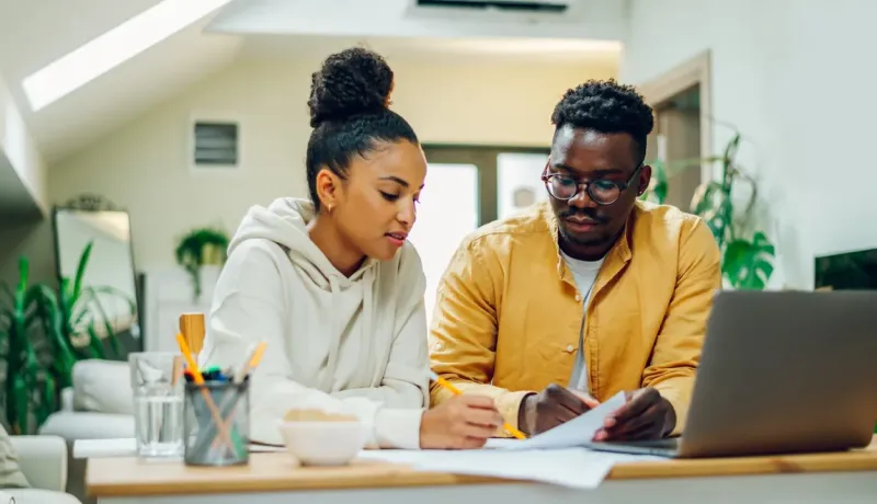 Jeune couple discutant des documents et utilisant un ordinateur portable à la maison.