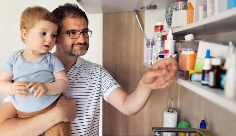 Un père et son enfant en bas âge cherchent des médicaments dans une armoire à pharmacie.