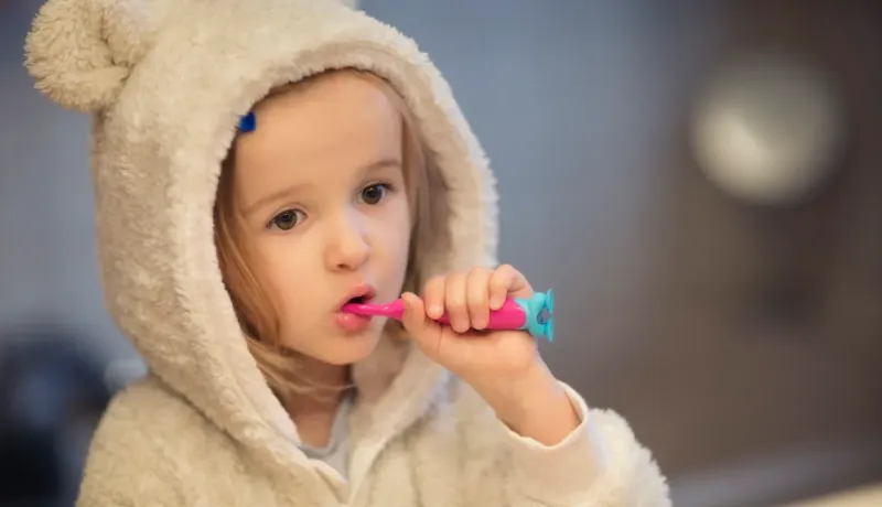 Petite fille brossant ses dents, portant un peignoir à capuche d'animal.
