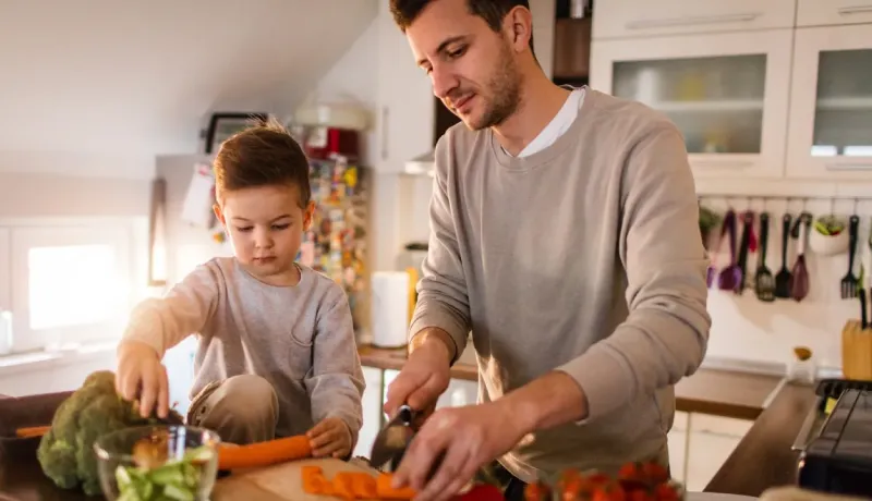 Un père et son jeune enfant coupent des légumes ensemble dans la cuisine.