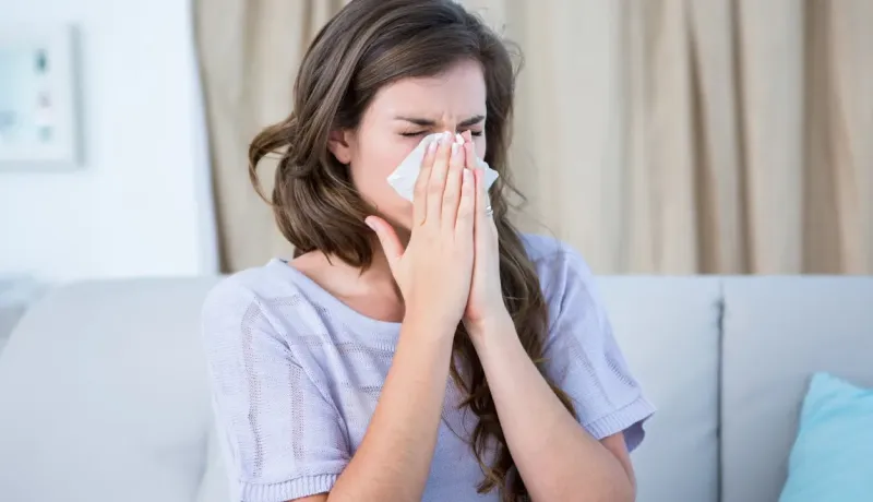 Une femme éternue dans un mouchoir, les yeux fermés, potentiellement liée à une congestion nasale ou une rhinite allergique.