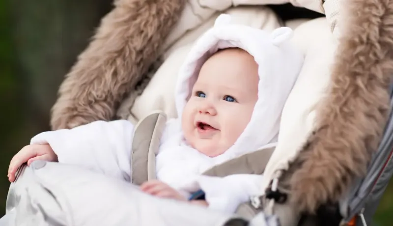Un bébé souriant est confortablement installé dans une poussette, portant une combinaison douillette.