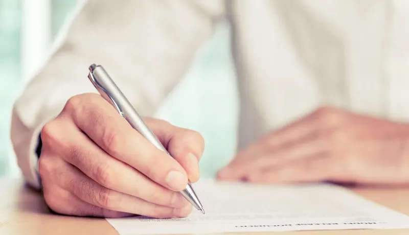 Gros plan sur une main d'homme écrivant avec un stylo sur un document.