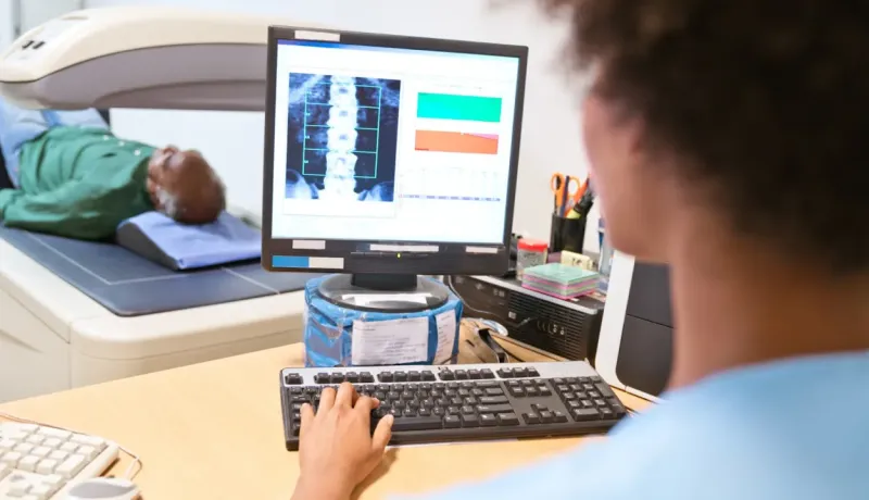 Un professionnel de la santé examine les résultats d'un scanner de densitométrie osseuse sur un écran d'ordinateur.