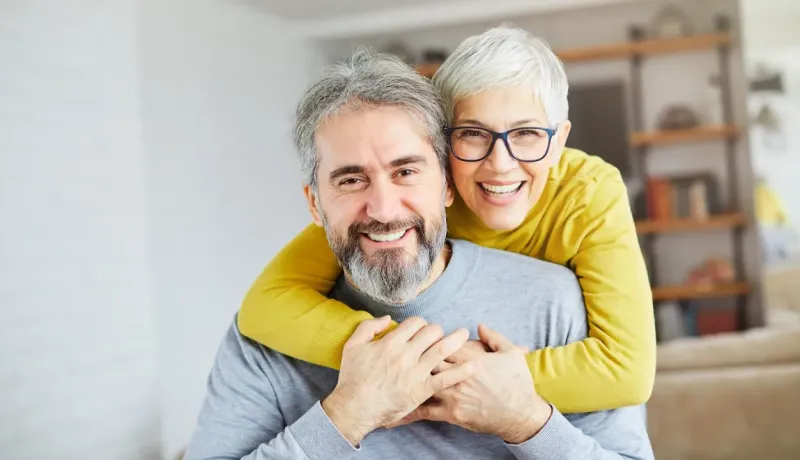 Un couple de personnes âgées souriantes, la femme étreignant l'homme par derrière.