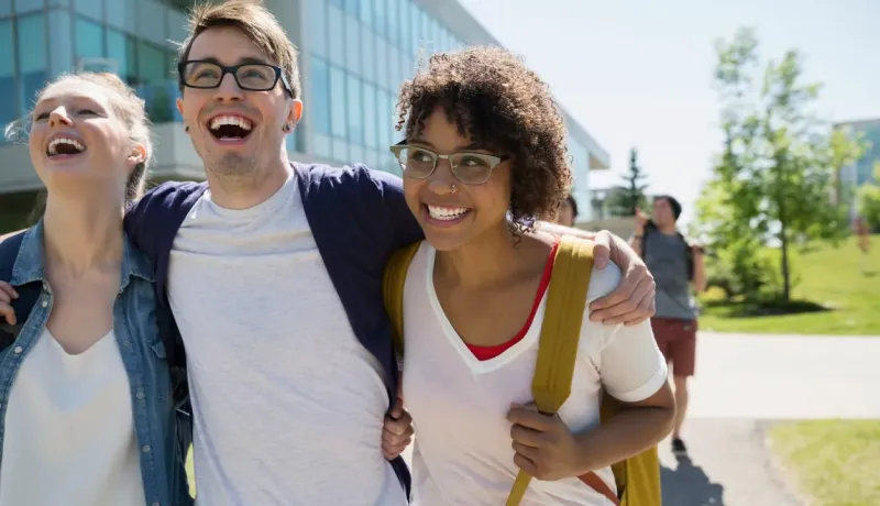 Trois jeunes amis souriants et riants, les bras autour des épaules, marchant ensemble à l'extérieur.