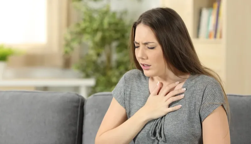 Une femme à la maison, visiblement mal à l'aise, se tenant la poitrine avec une expression de douleur.