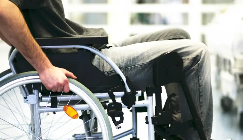 Gros plan sur un homme en fauteuil roulant, se déplaçant en poussant les roues.