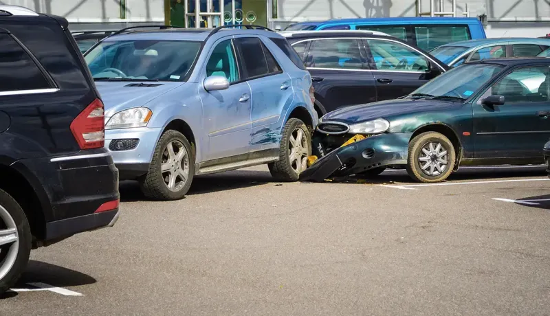 Deux voitures endommagées après un accident dans un parking, une SUV bleue et une berline verte.