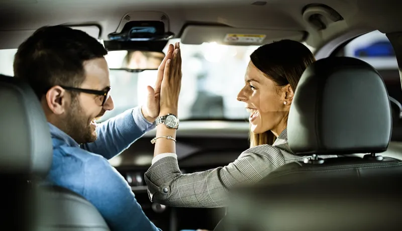 Un homme et une femme souriants se font un high-five à l'intérieur d'une voiture, vus depuis l'arrière.
