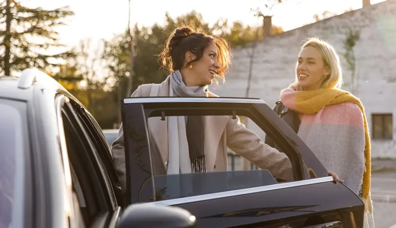 Deux femmes souriantes près d'une voiture, l'une ouvrant la portière.