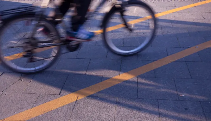 Un cycliste en mouvement sur une piste cyclable pavée avec une ligne jaune, créant un effet de flou dynamique.