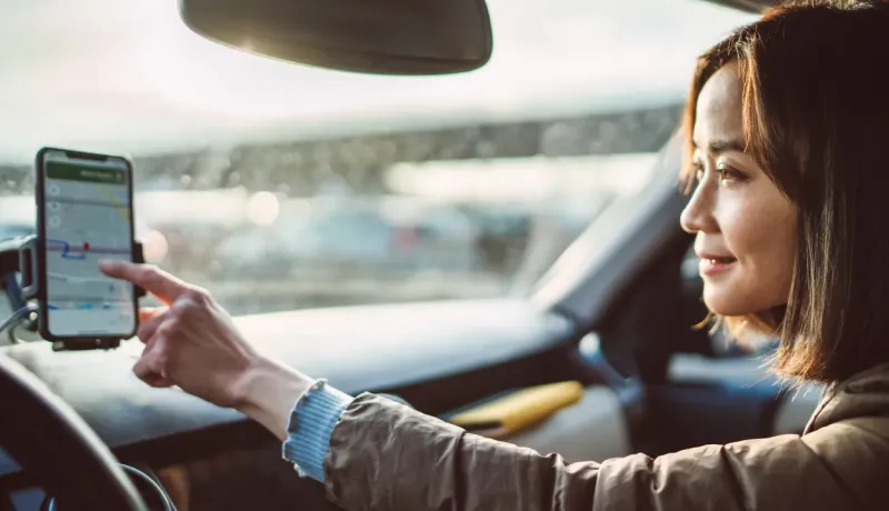 Une femme conduit une voiture en utilisant un smartphone pour la navigation.