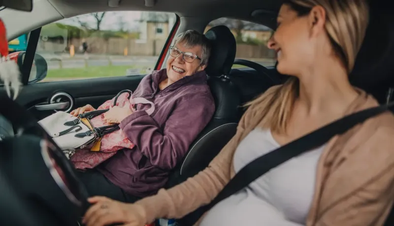 Deux femmes souriantes sont dans un véhicule. La passagère, plus âgée, s'apprête à sortir du véhicule.
