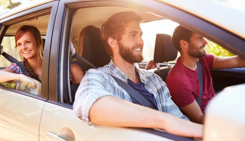 Quatre jeunes amis souriants et joyeux voyagent ensemble en voiture par une journée ensoleillée, profitant de leur trajet.