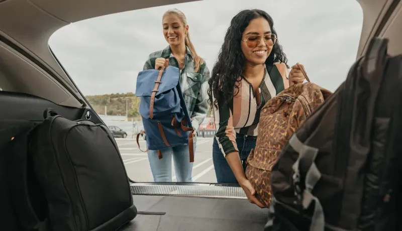 Deux femmes chargent leurs bagages dans le coffre d'une voiture.
