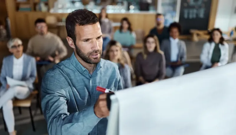 Un expert en sécurité routière écrit sur un tableau, tandis que ses stagiaires l'écoutent attentivement.