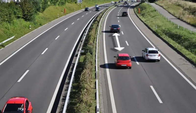 Une autoroute ensoleillée avec plusieurs voitures circulant, des flèches blanches indiquant la distance de sécurité.