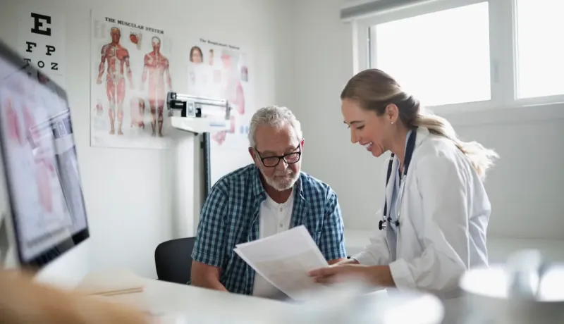 Un médecin souriant et un homme âgé examinent des documents dans un bureau médical.