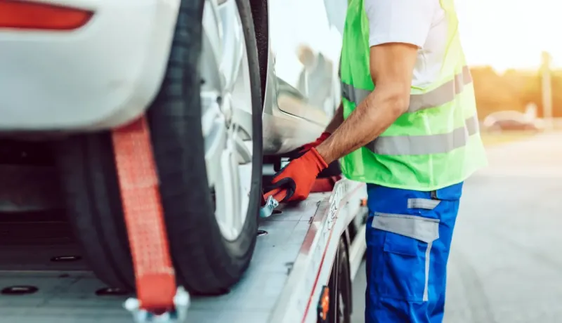 Un homme en gilet de sécurité fluo et gants rouges attache une voiture sur une dépanneuse.