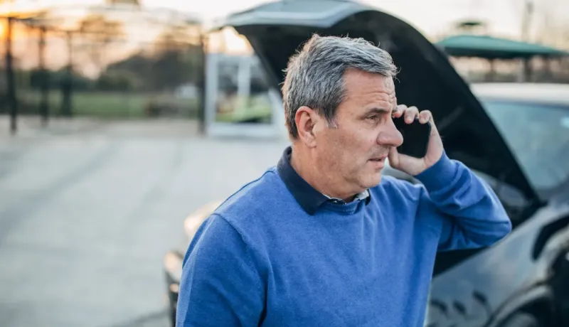 Un homme appelle au téléphone devant le capot ouvert d'une voiture en panne.