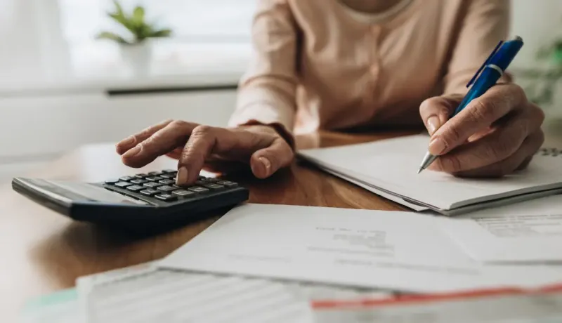 Gros plan sur des mains féminines utilisant une calculatrice tout en prenant des notes.
