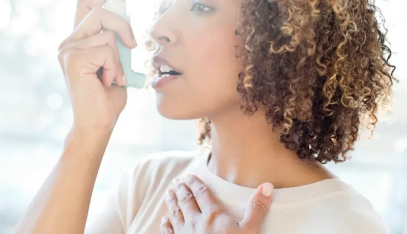 Gros plan d'une femme aux cheveux bouclés utilisant un inhalateur pour soulager une crise d'asthme.