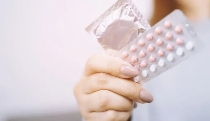 Gros plan sur une main tenant un préservatif et une plaquette de pilules contraceptives.