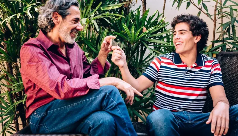 Un homme plus âgé souriant partage un préservatif à son fils, assis dehors.