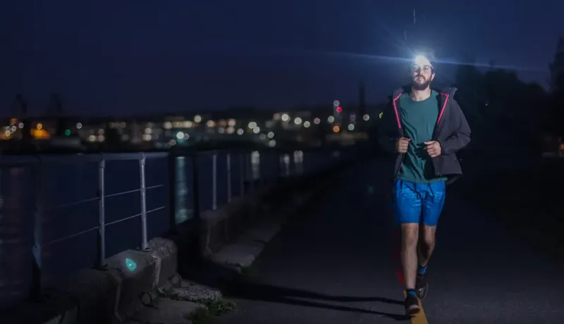 Un homme court la nuit avec une lampe frontale le long d'un chemin éclairé.