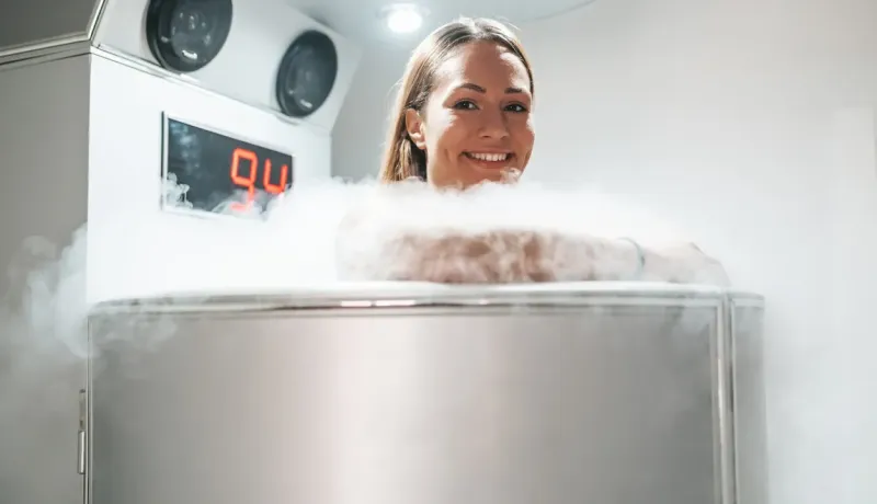 Une femme souriante dans une cabine de cryothérapie, entourée de vapeur froide.