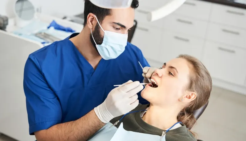 Un dentiste masqué effectue un examen dentaire sur une patiente.
