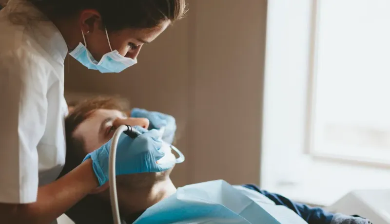 Un dentiste masqué et ganté effectue un examen dentaire sur un patient allongé.